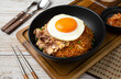 Closeup of Kimchi rice with grilled brisket sliced and fried egg in black bowl on wooden table.