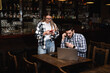 © Srdjan - Two Diverse Entrepreneurs Have a Team Meeting in Their Stylish Coffee Shop. Barista and Cafe Owner Discuss Work Schedule and Menu on Mobile or Computer. Young Female and Male Restaurant Employees