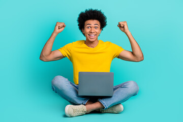 Wall Mural - Full body photo of delighted excited person sit floor raise fists use netbook isolated on turquoise color background