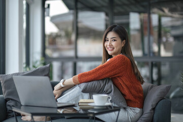 Wall Mural - asian young woman listening music with headphone and streaming music from laptop on sofa relaxing at home