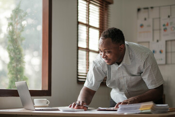 Wall Mural - Portrait of handsome African black young business man working on laptop at office desk