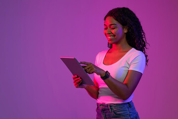 Poster - Smiling Black Female Using Digital Tablet While Standing In Neon Light