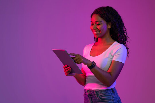 Wall Mural - Smiling Black Female Using Digital Tablet While Standing In Neon Light
