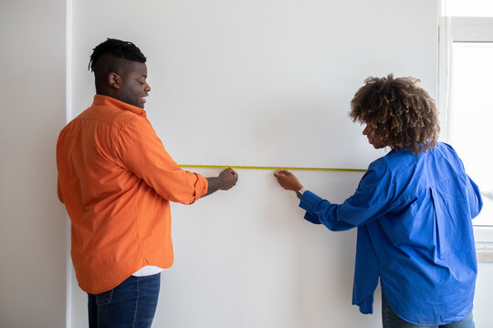 black couple measuring wall with tape ruler while making repairing at home