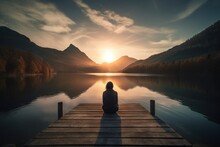  A Person Sitting On A Dock Looking Out At A Lake And Mountains In The Distance With The Sun Setting Over The Mountains In The Distance.  Generative Ai
