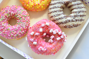 Wall Mural - A group of pink, yellow and chocolate donuts with sprinkles in cartoon box, top view