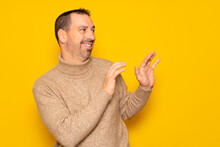 Bearded Hispanic Man In A Turtleneck Ducking To The Side In Embarrassment, Tries To Push Away From Something Or Someone With His Hands. Isolated On Yellow Background.