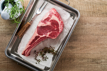 Wall Mural - Fresh tomahawk raw steak. Dry aged raw tomahawk beef steak with herbs and salt on old wooden background. Preparing to grill.  Top view and copy space.