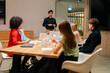© dikushin - Wide shot of professional male speaker giving corporate presentation for diverse businesspeople at meeting room, presents new business plan. Startup team sitting at boardroom at office listening boss.