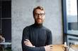 A young red-haired guy, a programmer or an entrepreneur in glasses, in a stylish cafe Looks at the camera and smiles. Freelancer works remotely. Online communication. small business.