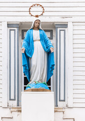 Fairbanks, Alaska, USA - July 27, 2011: Closeup, Virgin Mary statue above entrance to historic white wooden Immaculate Conception Catholic church. She stands on blue globe with fishes