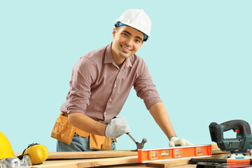 Poster - Young carpenter with hammer and wooden planks at table on blue background