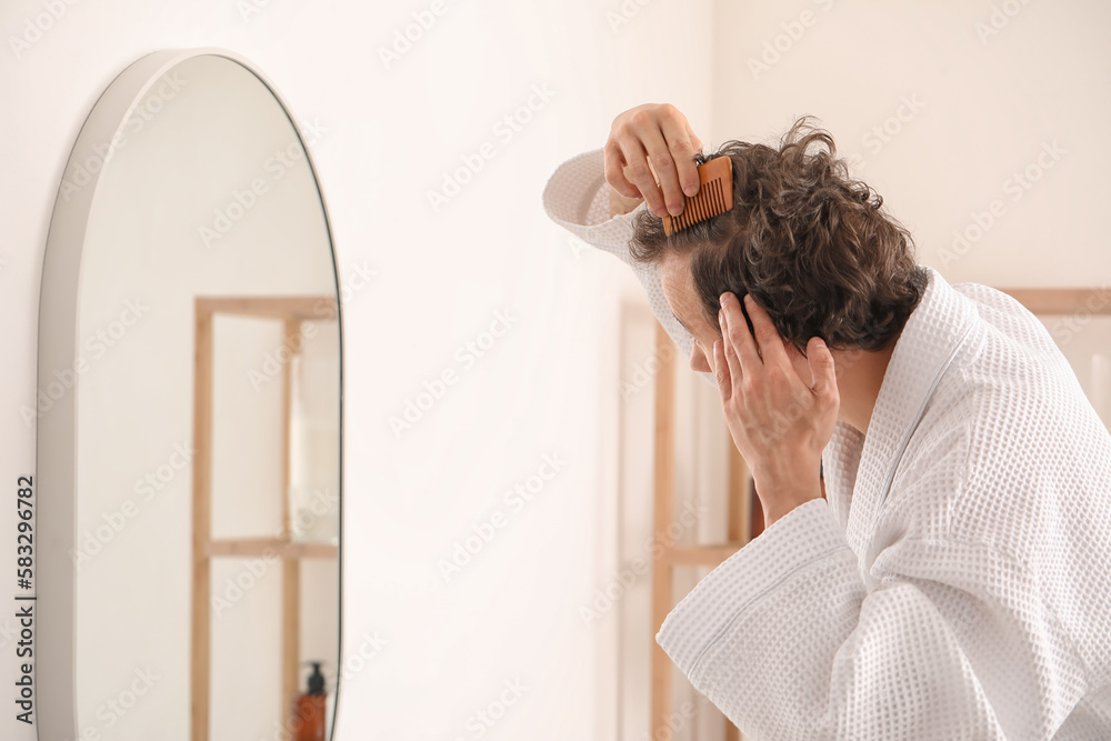 Young man combing hair near mirror in bathroom