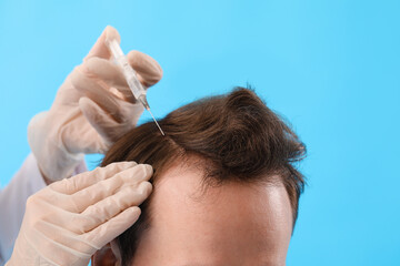 Wall Mural - Young man receiving injection for hair growth on blue background, closeup