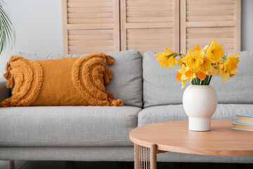 Vase with narcissus flowers on coffee table in living room