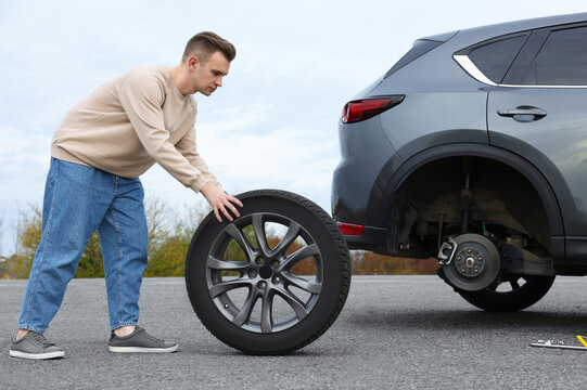 Wall Mural - Young man changing tire of car on roadside