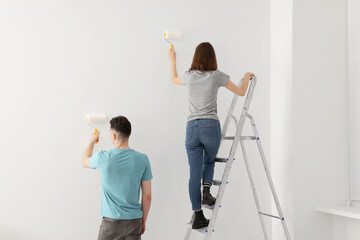 Poster - Young man and woman painting wall with rollers indoors. Room renovation