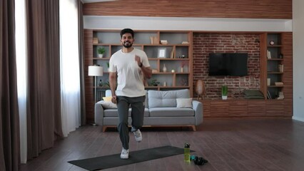 Wall Mural - Handsome arabian man in short clothes making active fitness exercises at living room. Young bearded guy training muscles for fit body shape. Healthy lifestyles concept.