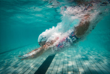 A talented female swimmer dives into a full-size tournament pool to train or compete. This stunning wide-angle underwater photo captures the grace and power of this athlete in action.