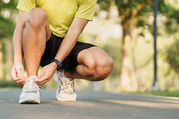 Wall Mural - Young athlete man tying running shoes in the park outdoor, male runner ready for jogging on the road outside, asian Fitness walking and exercise on footpath in morning. wellness and sport concepts