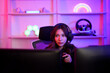 © MergeIdea - Asian young gamer girl watching and thinking about strategy game before clear to the next stage level in neon entertainment room