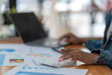 Wall Mural - Business woman calculating monthly expenses, managing budget. Woman sitting at table using calculator to calculate tax refund, working at office with laptop computer on table, close up.