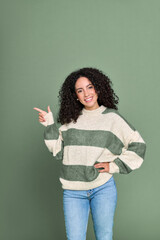 Wall Mural - Young happy latin woman pointing finger aside isolated on green background. Smiling female model showing advertising sale offer presenting promotion commercial ad discounts concept. Vertical