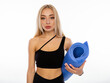 © oleg_ermak - Caucasian woman with long blond hair in black sportswear hold yoga mat or mat for fitness poses on a white background and shows perfect body. Personal care and sports at home.