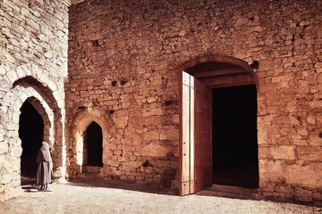 Wall Mural - Medieval door in stone courtyard under scorching sun with monk in gray cloak., created with generative ai