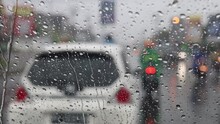 Rain Falling On Car Windshield View. Drive Car On Traffic Jam Street At Heavy Rain Storm, Inside A Car Driving, Defocused Traffic Light Background