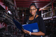 woman African American warehouse inspector wear spectacles crossed arms holding clipboard standing in factory auto parts. female employee business warehouse motor vehicle.