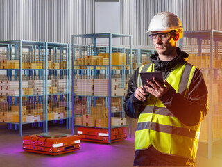 Poster - Employee of modern warehouse. Man storekeeper. Robotization fulfilment of process. Cart-robots for moving racks. Storekeeper controls robots through phone. Man in storage room. Agv and amr robots