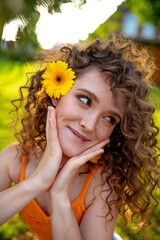 portrait of a girl with curly hair with a flower in her hair against a background of lush green grass. Sunflower in hair. Flowers in hair. Curly hair.