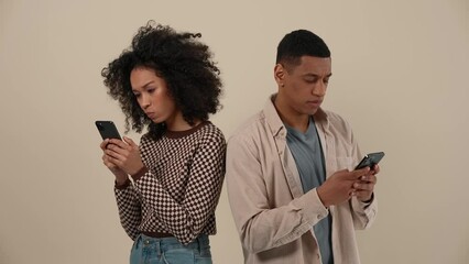 serious african young couple texting on phones while standing in the beige studio