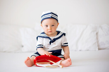 Wall Mural - Cute baby boy, dressed in marine clothes, playing with wooden boat