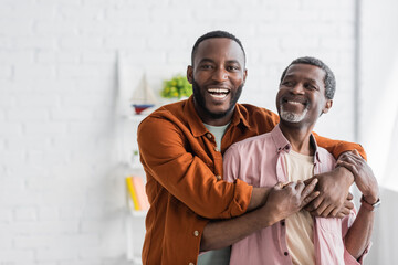 cheerful african american man hugging mature dad and looking at camera at home.