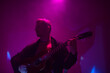 © astrosystem - Musician playing acoustic guitar in a foggy club with colorful lights.