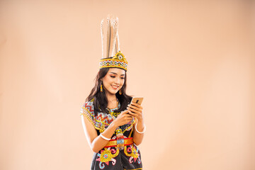 asian woman in traditional clothes of dayak tribe smiling while using the phone on isolated background