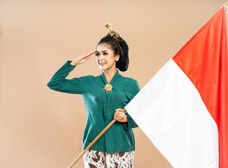 Wall Mural - asian woman in green kebaya standing looking right with salutation and holding the indonesian flag on isolated background