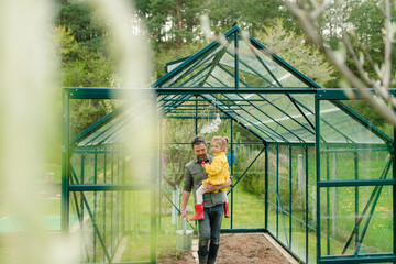 Wall Mural - Father holding his little daughter in feco greenhouse,taking care of vegetable together, sustainable lifestyle.