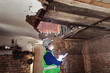 © Siniehina - Building inspector. Man in a hard hat and a yellow reflective vest examines damaged structures and inspects the building. Damage assessment. Preparing for the repair or construction of a building