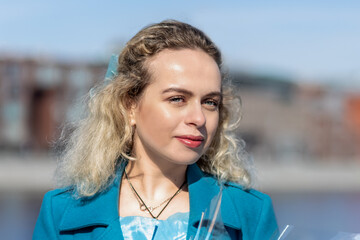 A young blonde woman in a blue coat stands with a bouquet of colorful gypsophila on the embankment in the park. The concept of the spring holiday - March 8, Easter, Women's Day