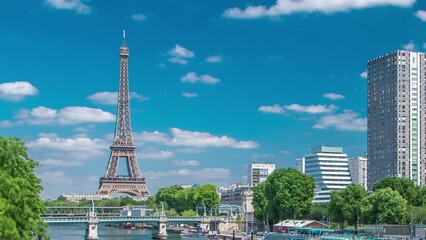 Canvas Print - Eiffel tower and modern buildings at the river Seine waterfront timelapse from Grenelle bridge in Paris, France. Isle of the Swans and ship on river at sunny summer day