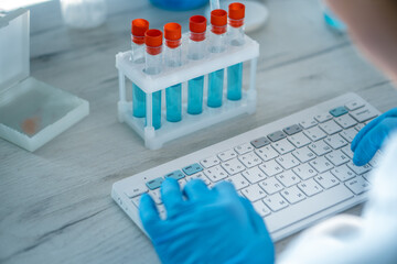 Aufkleber - A female researcher sits at a workplace in a laboratory, behind a personal computer monitor. Against the background research statistics. Pharmaceutical medical worker in protection works at keyboard.