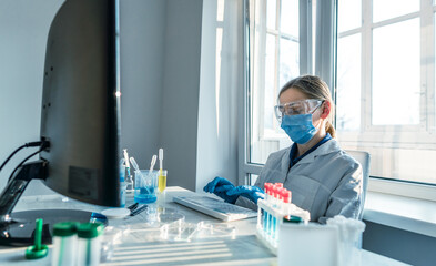 Aufkleber - A female researcher sits at a workplace in a laboratory, behind a personal computer monitor. Against the background research statistics. Pharmaceutical medical worker in protection works at keyboard.