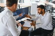 © Serhii - Two men traders sitting at desk at office together monitoring stocks data candle charts on screen analyzing price flow smiling cheerful having profit teamwork concept