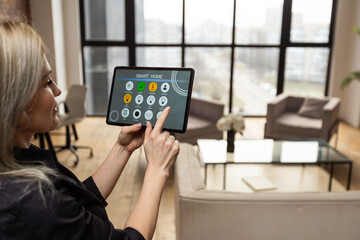 Poster - young woman using smart home app to control light turning on with tablet pc