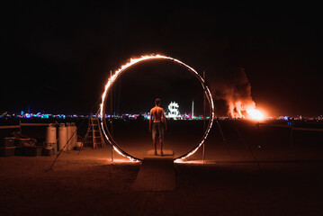 Wall Mural - A man standing in the circle of fire at Burning Man. Beautiful music festival in a desert.at night at the Burning Man Festival.