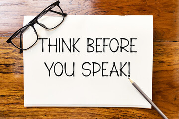 Think before you speak text on blank notebook paper on wooden table with pencil and glasses aside. Business concept and legal concept about thinking before speaking.