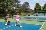 Fototapeta  - Two players approach the net in a competitive doubles game of pickleball on a blue and green court in summer.